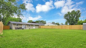 A fenced backyard with a house, a wooden deck, and a grassy lawn.