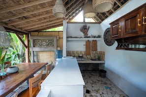 A kitchen with a long white countertop, wooden cabinets, hanging lights, and a decorative wall piece. - Jungle valley 3 bedroom Private pool (Ubud)