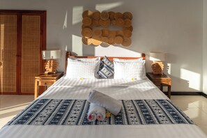 A neatly made bed with a patterned bedspread, two bedside tables with lamps, and a wall decorated with circular wooden elements. - Jungle valley 3 bedroom Private pool (Ubud)