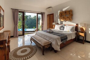 Ein Schlafzimmer mit einem großen Bett, einer Sitzbank, einem runden Teppich und Blick auf ein Schwimmbad durch eine Schiebetür.