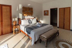 A bedroom with a bed, bedside tables, a bench, a wall-mounted decorative item, and a door. - Jungle valley 3 bedroom Private pool (Ubud)