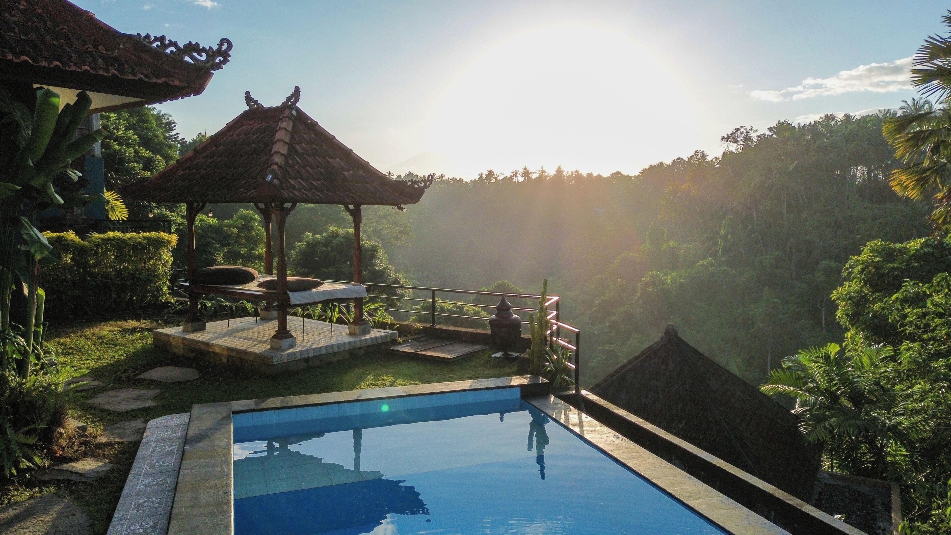 A swimming pool with a gazebo, surrounded by lush greenery and a mountainous backdrop.