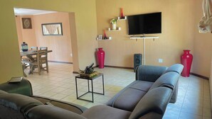 A living room with a sofa, TV, and a dining area with chairs and a table.