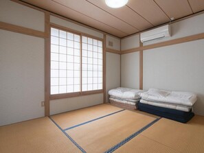 A traditional Japanese room with tatami flooring, a shoji screen window, and a futon bed.