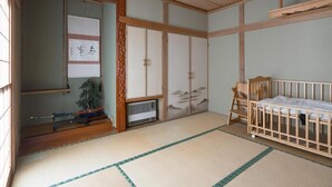 Una habitación japonesa tradicional con suelo de tatami, una cuna de madera, puertas correderas y un ventilador de techo.