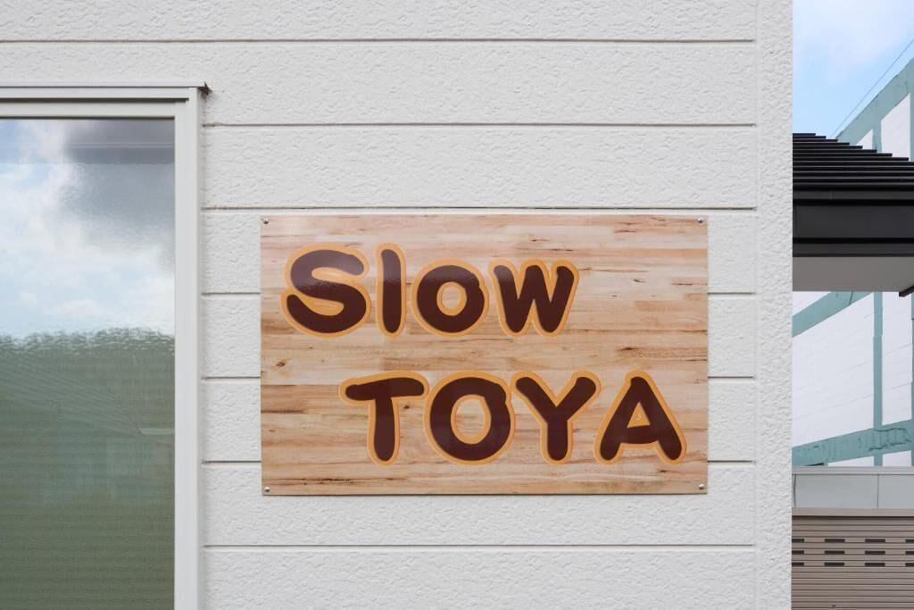 A wooden sign with the words 'SLOW TOYA' on a building wall.