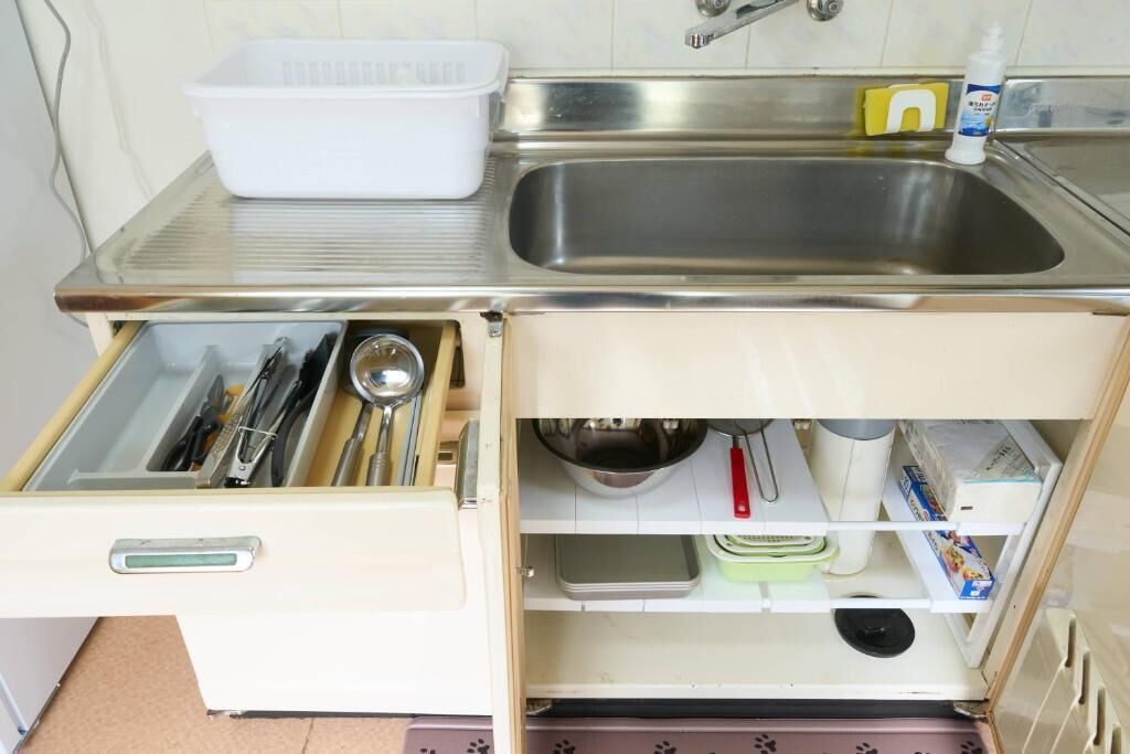 A kitchen with a stainless steel sink, a white plastic container, and a drawer with utensils.