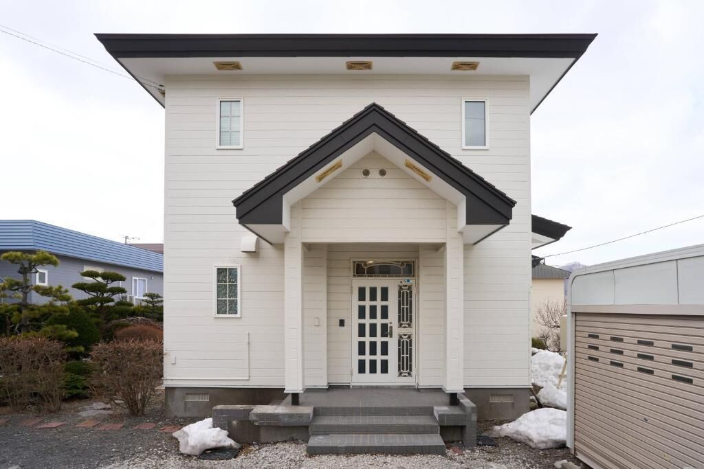 A two-story building with a white facade, a black roof, and a front entrance with a door and steps.