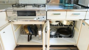 Cocina compacta con horno integrado, cafetera y diferentes utensilios y ollas guardados en un armario.