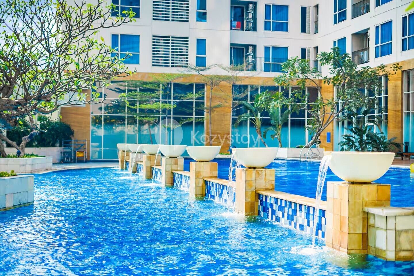 A swimming pool with multiple water features and a modern building in the background.