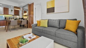 Un soggiorno moderno con un divano grigio, un tavolino in legno con una pianta e un'area pranzo con una cucina sullo sfondo.