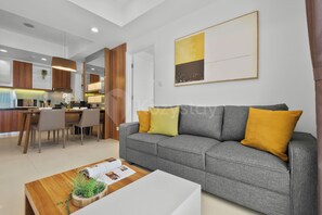 A modern living room with a grey sofa, a wooden coffee table with a plant, and a dining area with a kitchen in the background. - Astera by Kozystay - Kuningan (South Jakarta)