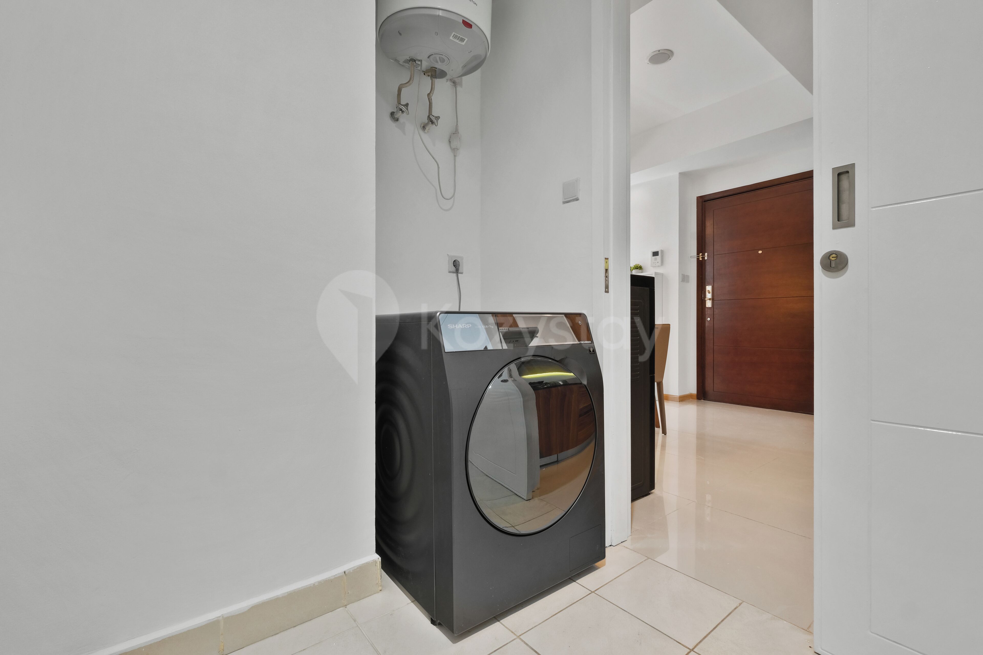 Een hal met een moderne, compacte was-droogcombinatie, een houten deur en een witte muur.