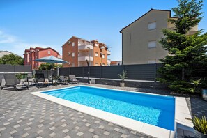 Ein rechteckiger Swimmingpool mit einer gefliesten Liegefläche, umgeben von Liegestühlen und einem Blumentopf.