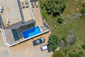 Eine Luftaufnahme eines Grundstücks mit Schwimmbad, zwei Autos und einer Terrassenanlage.
