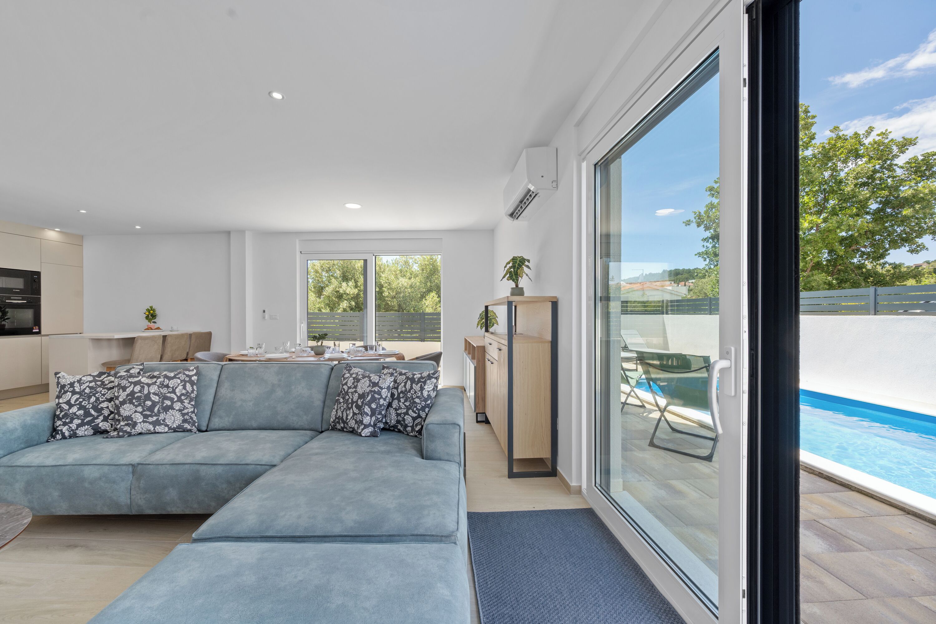 A modern living room with a sectional sofa, a dining area, and a view of a swimming pool.