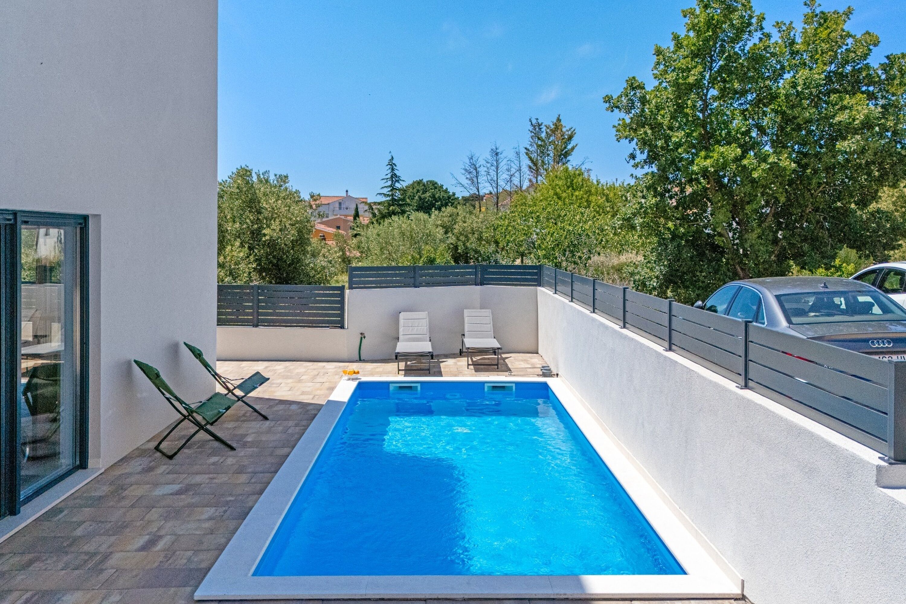 Ein rechteckiger Swimmingpool mit zwei Liegestühlen und einem Zaun.