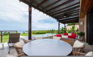 Ein überdachter Außenbereich mit Pool, Liegestühlen und Blick auf das Meer.