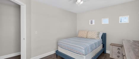 A bedroom with a bed, a ceiling fan, and a small window.