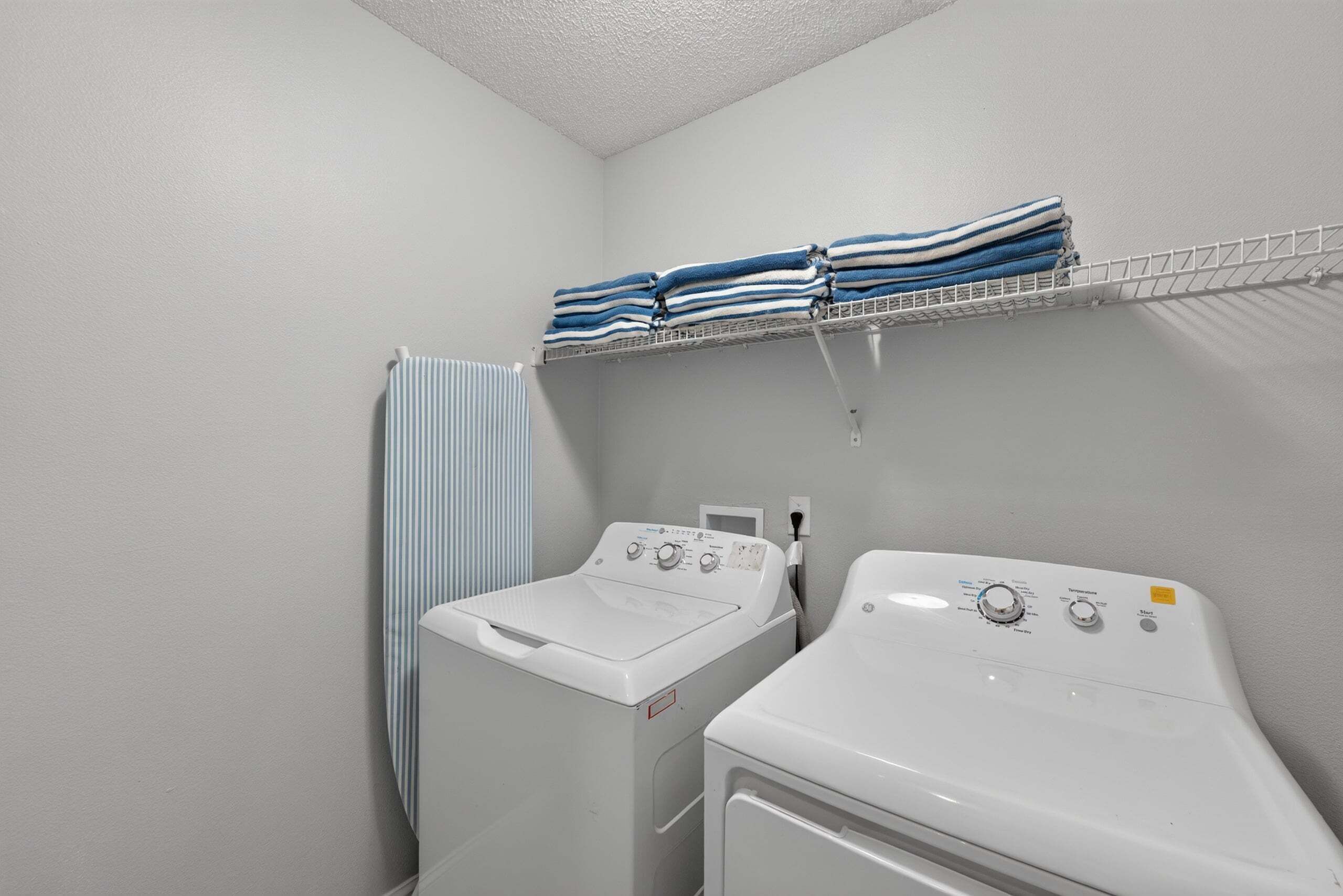 A laundry room with two washing machines, a drying rack with folded towels, and a striped towel hanging on a rack.