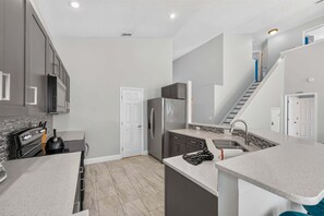 A modern kitchen with grey cabinets, a stainless steel refrigerator, and a built-in oven. - Spacious 5BR Pool Home Near Disney (Davenport)