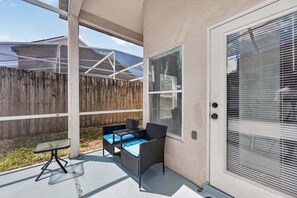 A covered patio area with a wicker table and chairs, a glass-top table, and a wooden fence in the background. - Spacious 5BR Pool Home Near Disney (Davenport)