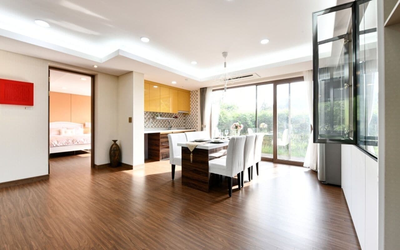 A modern kitchen with a dining area, wooden flooring, and large windows.