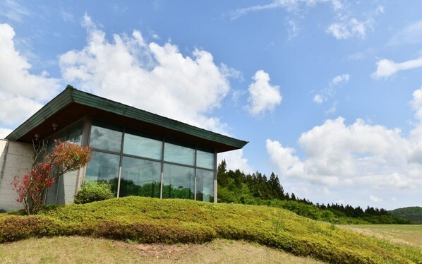 A modern building with large glass windows, surrounded by well-maintained hedges and a clear sky. - Jeju Tameus Golf & Village (Jeju City)