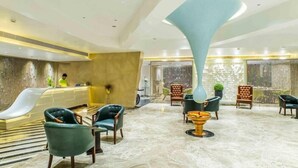 Eine Hotelhalle mit einer Rezeption, einer Sitzecke und einer großen dekorativen Leuchte.