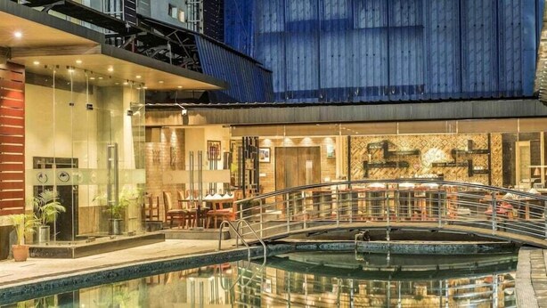 Ein Innenpoolbereich mit einer Brücke, Sitzgelegenheiten und einem Restaurant mit einem gemusterten Wanddesign.