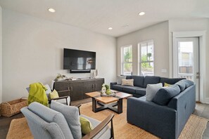 A modern living room with a sofa, armchairs, a coffee table, and a flat-screen TV mounted on the wall. - Boho-Chic House Near 30A Beach w/ Pool & Hot Tub (Santa Rosa Beach)