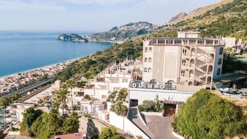 Hotel com terraço no telhado, vista para o mar e paisagem montanhosa ao fundo.