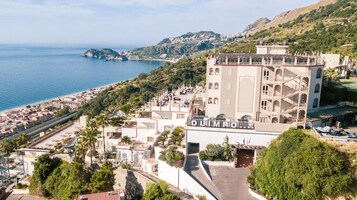Un hotel con terraza en la azotea, vistas al mar y un paisaje montañoso al fondo.