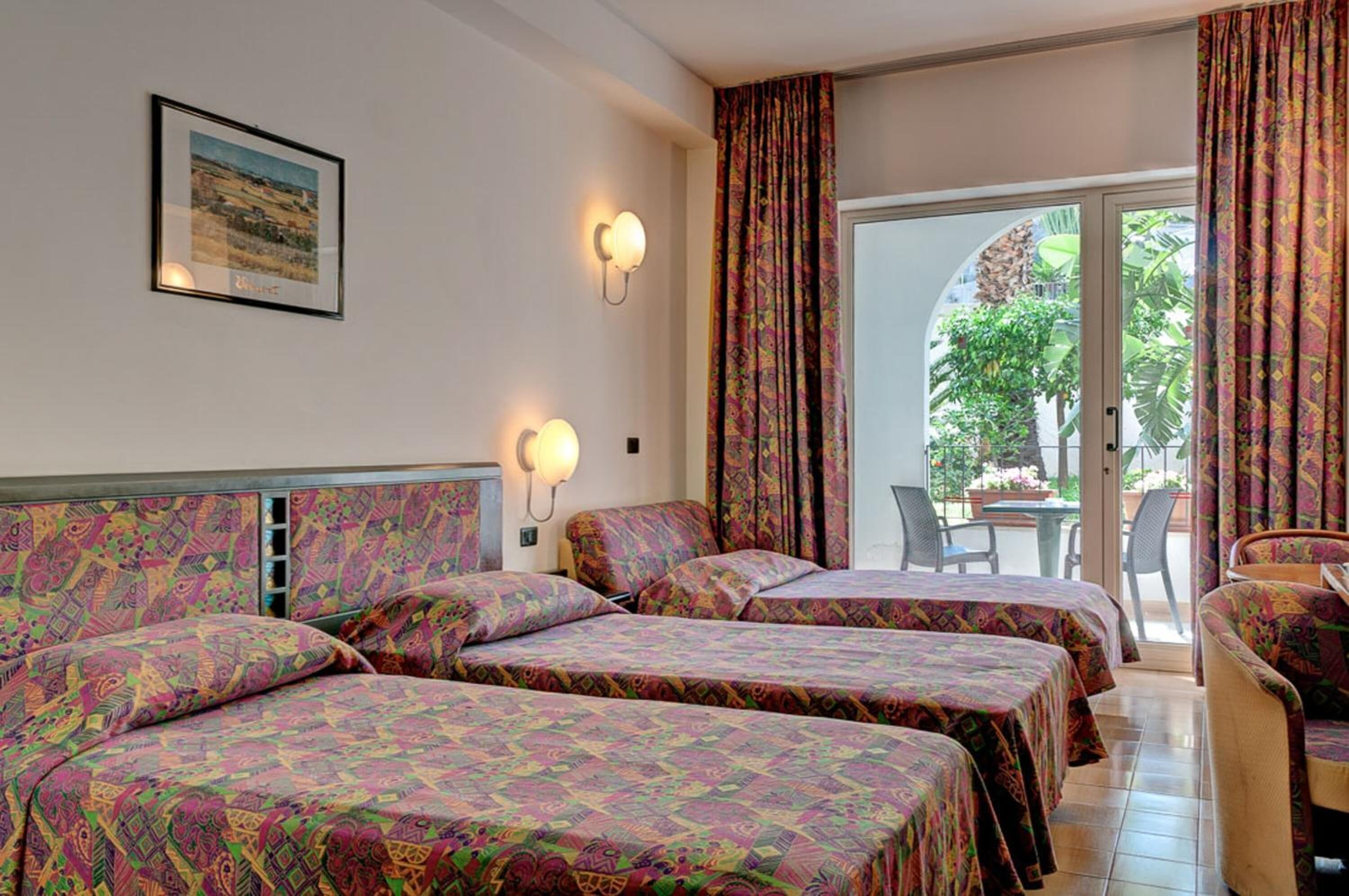 Quarto de hotel com duas camas, uma mesa, cadeiras e vista para o exterior.