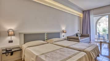 Quarto de hotel com duas camas, um sofá, uma mesinha e vista para o exterior.