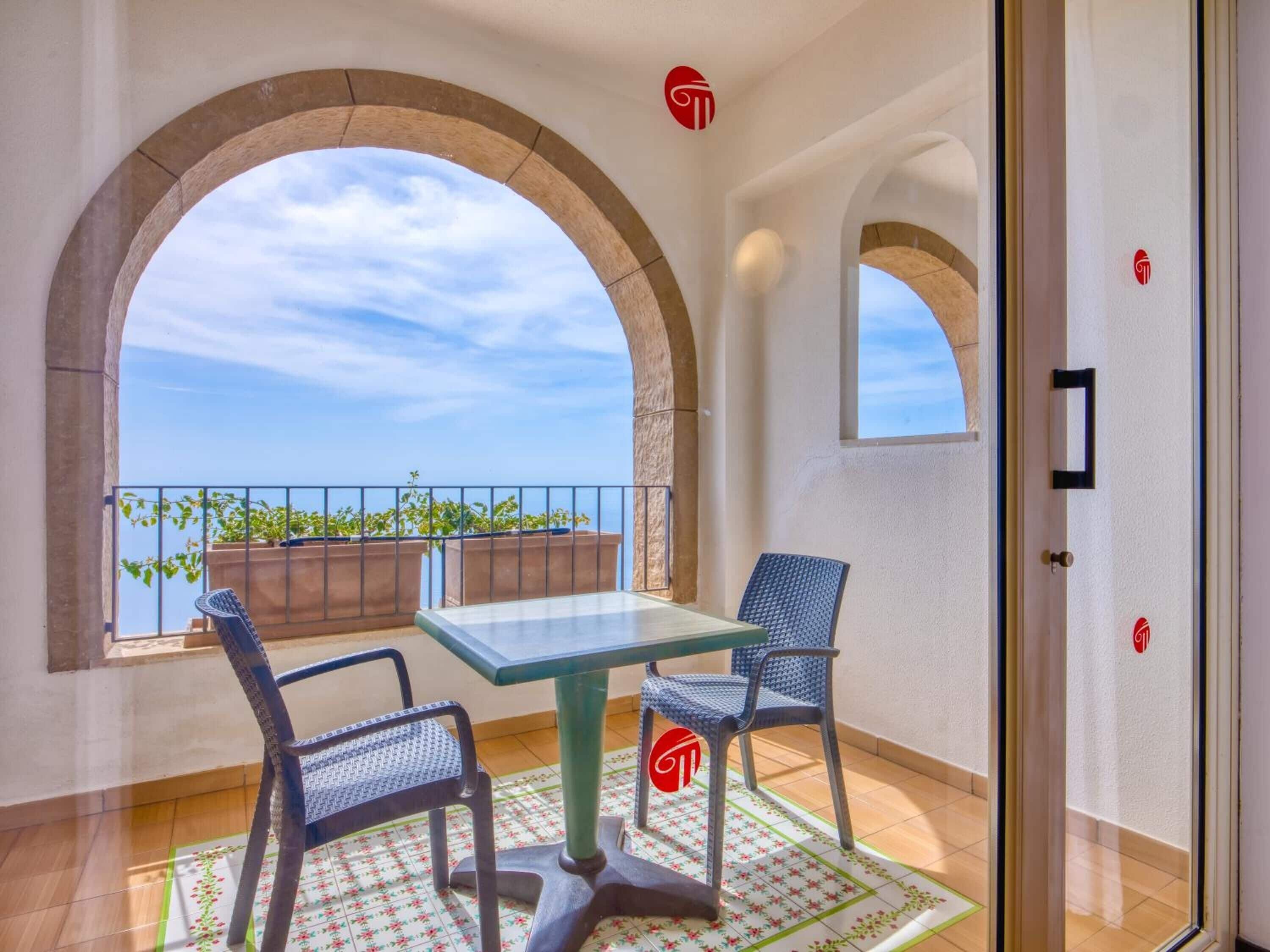 Un balcon avec une table et des chaises, une vue sur la mer et une porte ornée d’un logo.