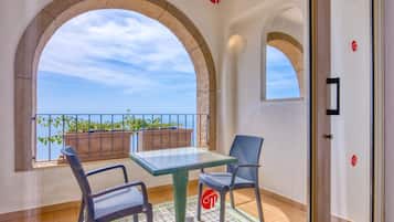 Un balcon avec une table et des chaises, une vue sur la mer et une porte ornée d’un logo.