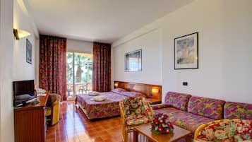 Une chambre d’hôtel avec un lit, un canapé, un bureau et une chaise. Il y a une fenêtre avec des rideaux, un tableau au mur et une plante sur la table.