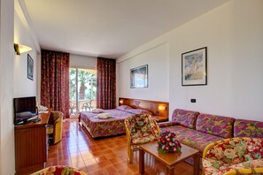 A hotel room with a bed, a sofa, a desk, and a chair. There is a window with curtains, a picture on the wall, and a plant on the table. - Olimpo & Le Terazze (Letojanni)