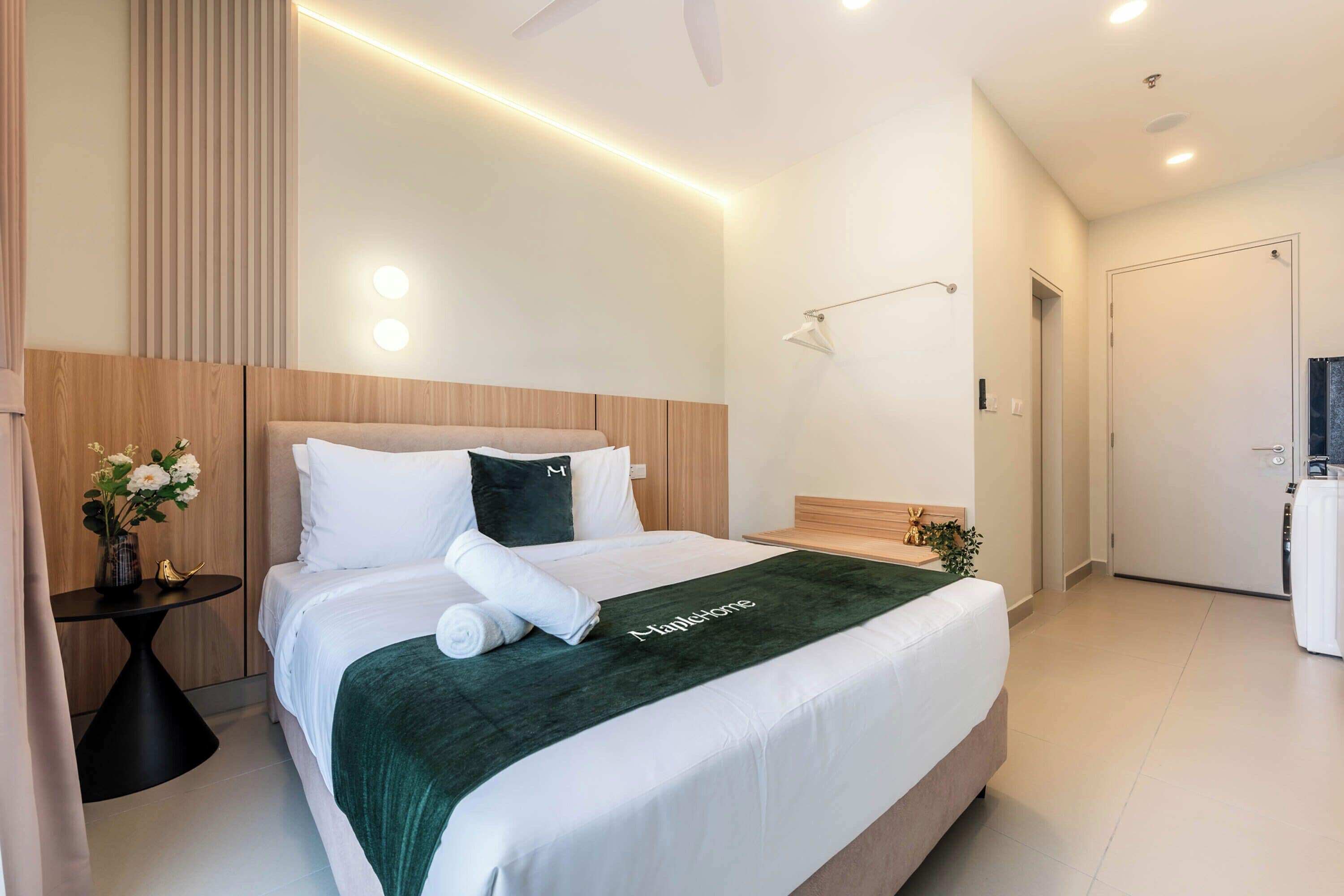 A modern hotel room with a large bed, bedside tables, a nightstand, a wall-mounted lamp, and a door leading to a bathroom.