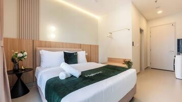 A modern hotel room with a large bed, bedside tables, a nightstand, a wall-mounted lamp, and a door leading to a bathroom.