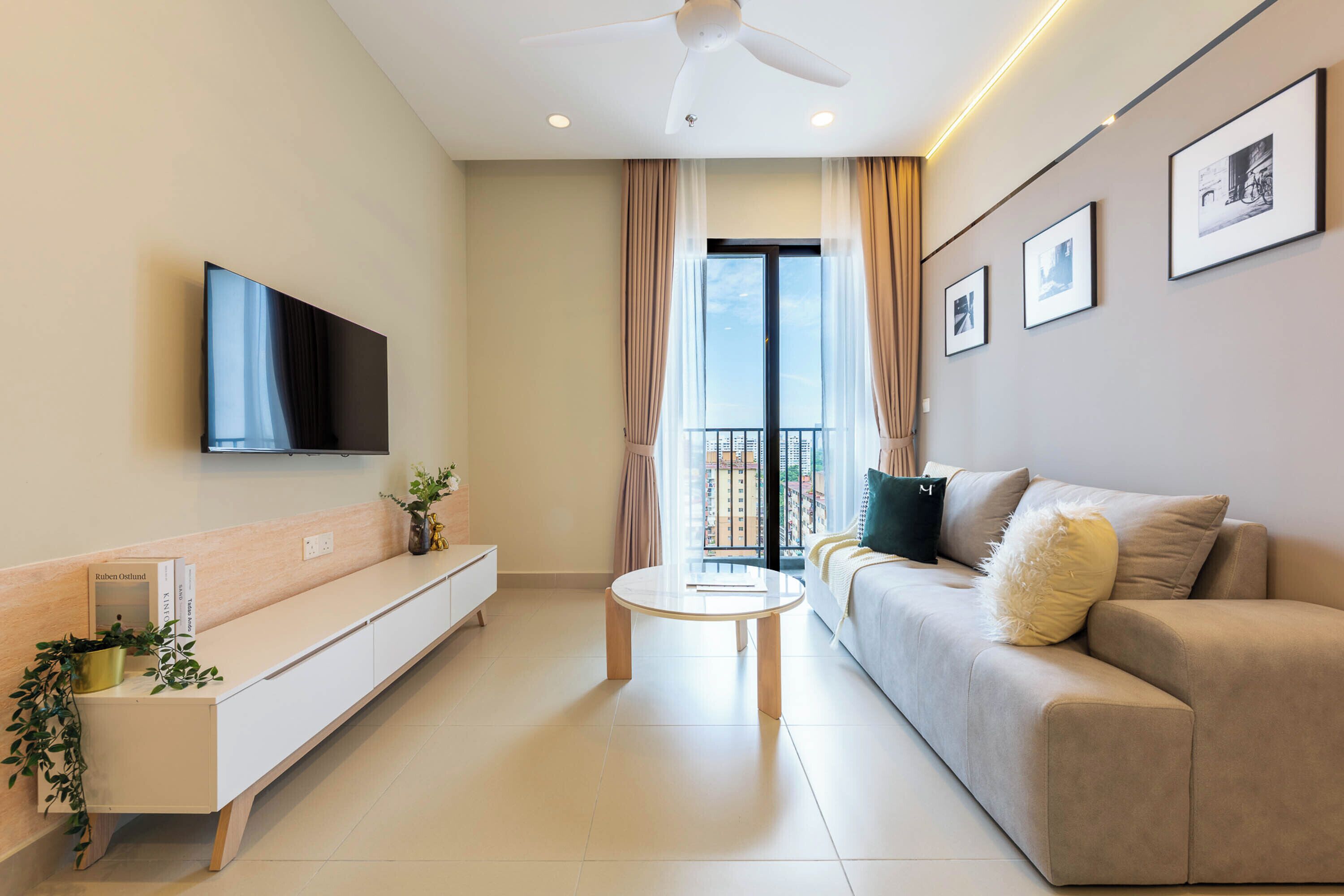 A modern living room with a flat-screen TV, a sofa, a coffee table, and a balcony with curtains.