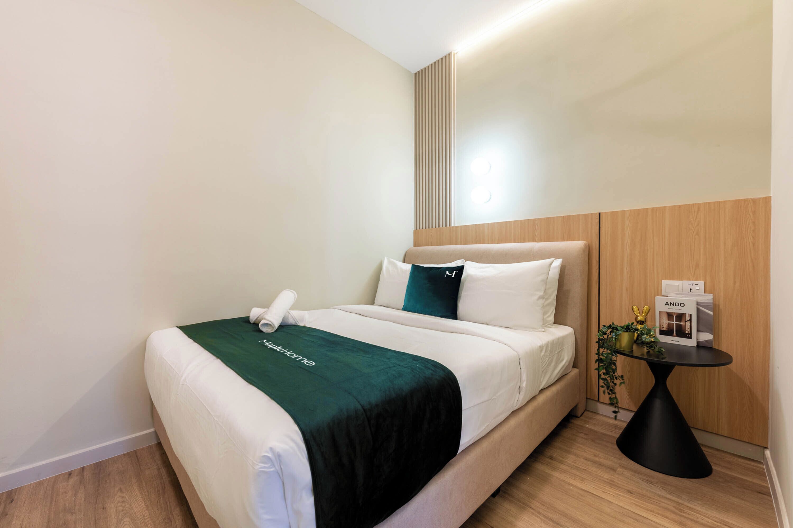 A hotel room with a bed, a bedside table with a lamp, and a small potted plant.