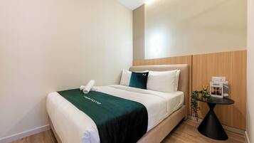 A hotel room with a bed, a bedside table with a lamp, and a small potted plant.