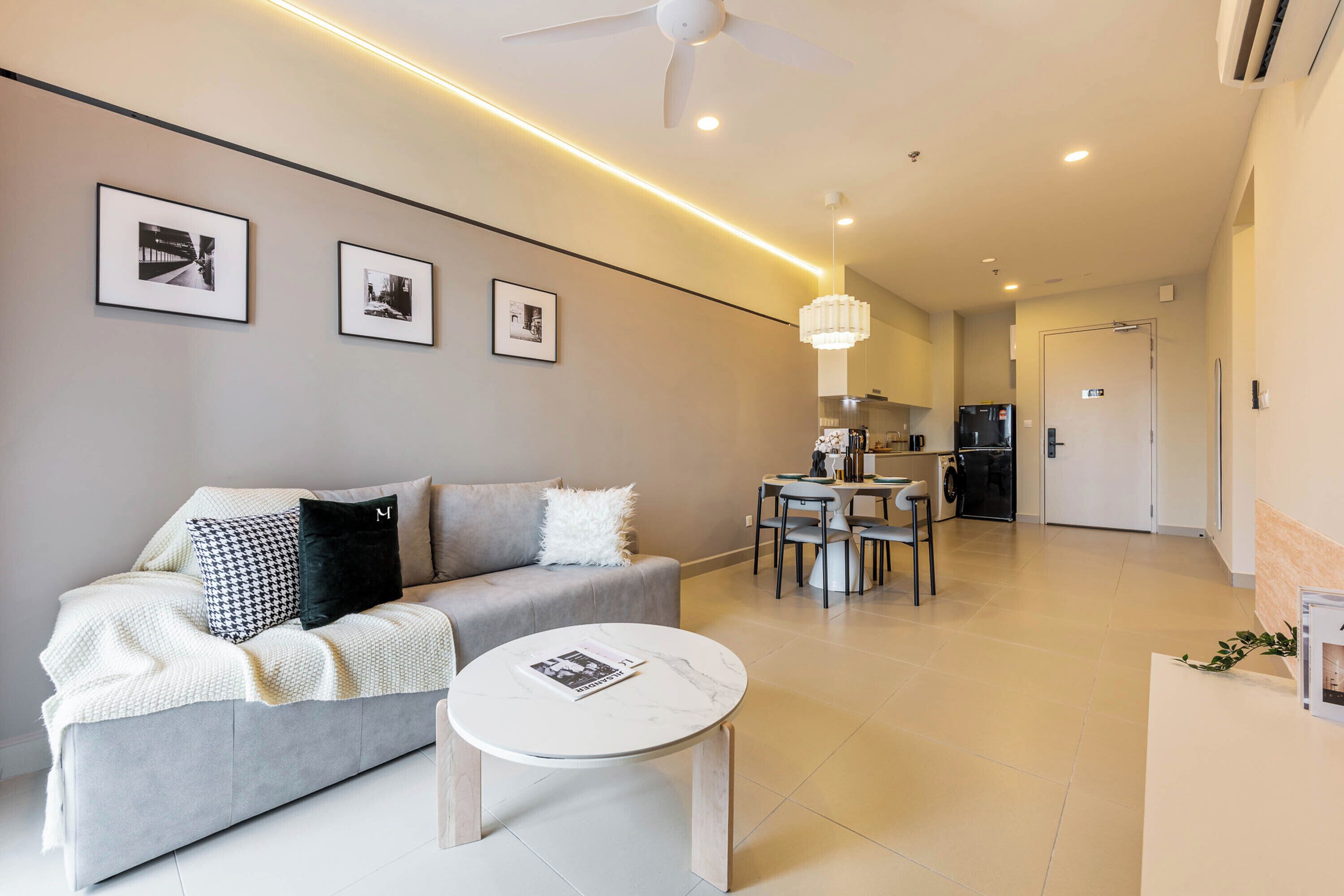 Un salon moderne avec un canapé gris, une table basse ronde et un coin repas comprenant une table et des chaises.