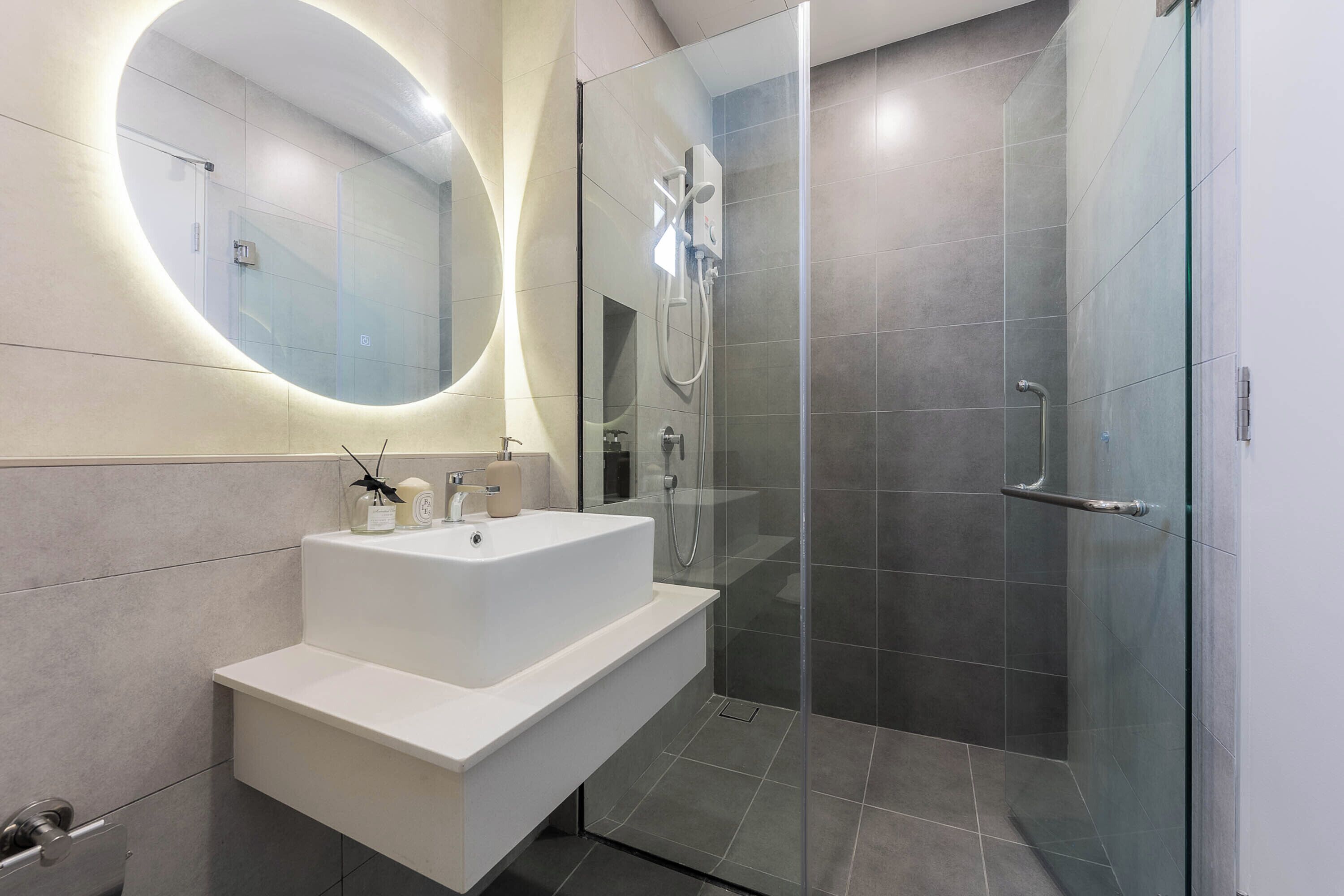 A modern bathroom with a large mirror, a white sink, and a glass-enclosed shower.