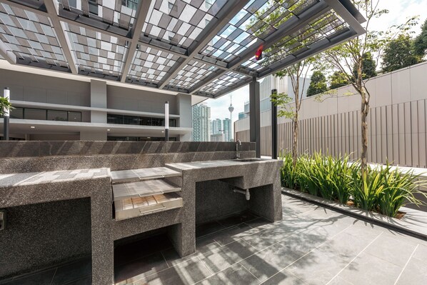 Un espacio de estar al aire libre con diseño moderno, que incluye una parrilla empotrada y una estructura de pérgola.