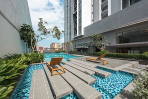 Un espace piscine extérieur moderne, doté de chaises longues et offrant une vue sur les bâtiments environnants.