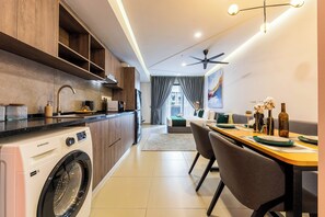 Une cuisine moderne équipée d’un lave-linge intégré, un coin repas avec une table et des chaises, et une vue sur le salon grâce à une porte vitrée.