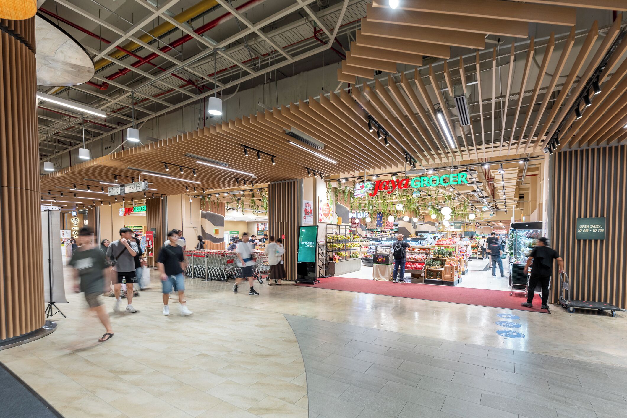 A shopping area with a grocer and a deli, featuring a modern ceiling design and a red carpet leading to the deli.
